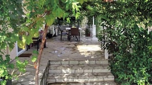 Une terrasse dallée de pierres, avec un banc et des chaises, entourée de verdure.
