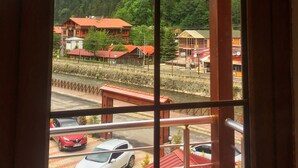 Vista a través de una ventana con celosía metálica, mostrando un paisaje montañoso con edificios y una carretera con automóviles estacionados.