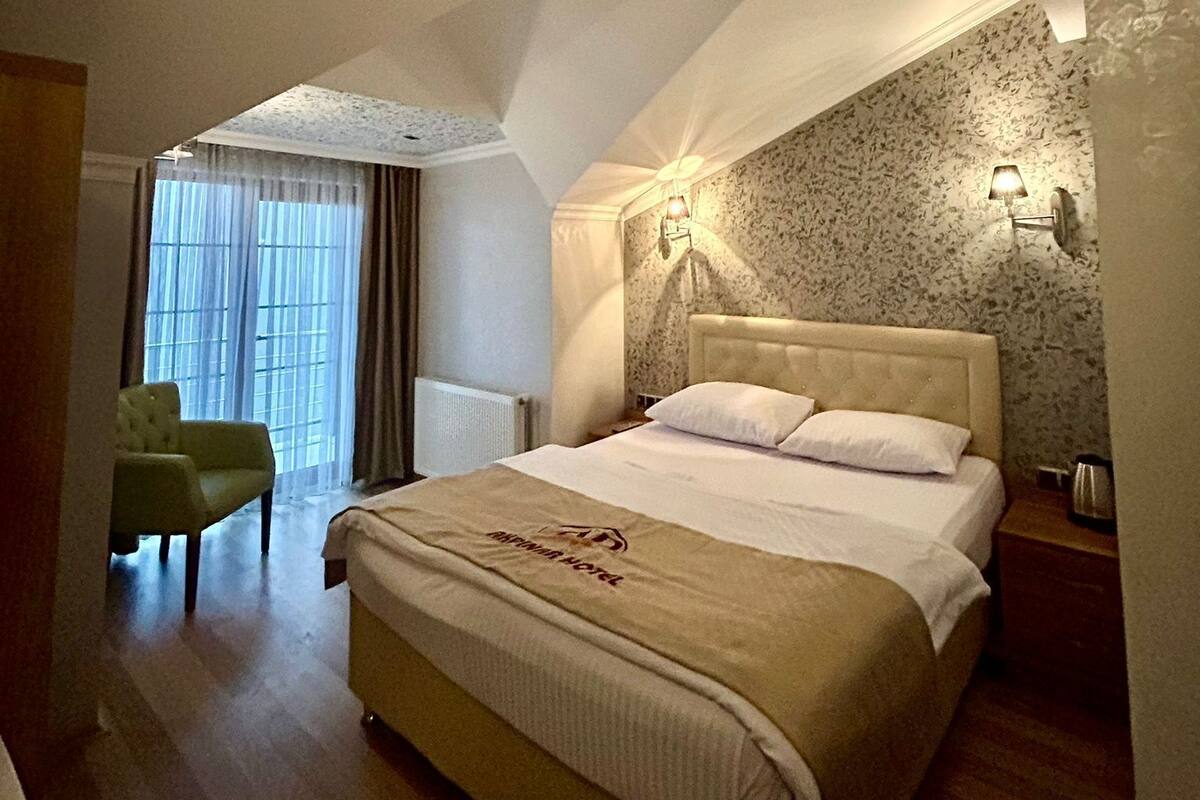 A bedroom with a bed, a chair, a radiator, and a window with curtains.