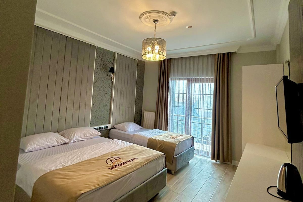 A hotel room with two beds, a desk, a TV, and a window with curtains.