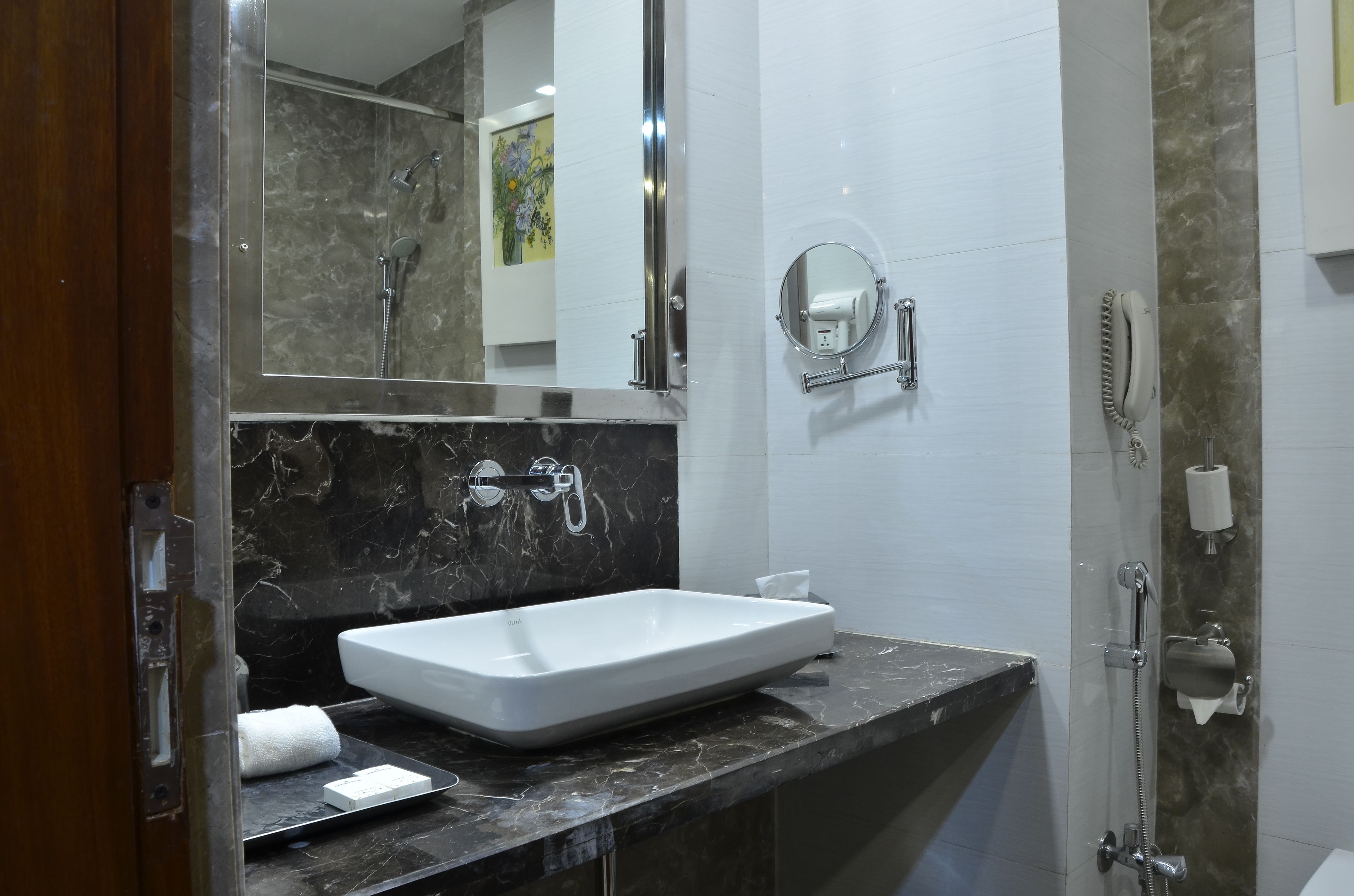 A bathroom with a white sink, a mirror, a handheld showerhead, and a towel dispenser.