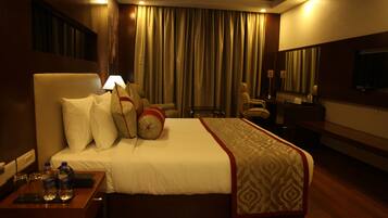 A hotel room with a large bed, a desk with a lamp, a chair, a TV, and a window with curtains.