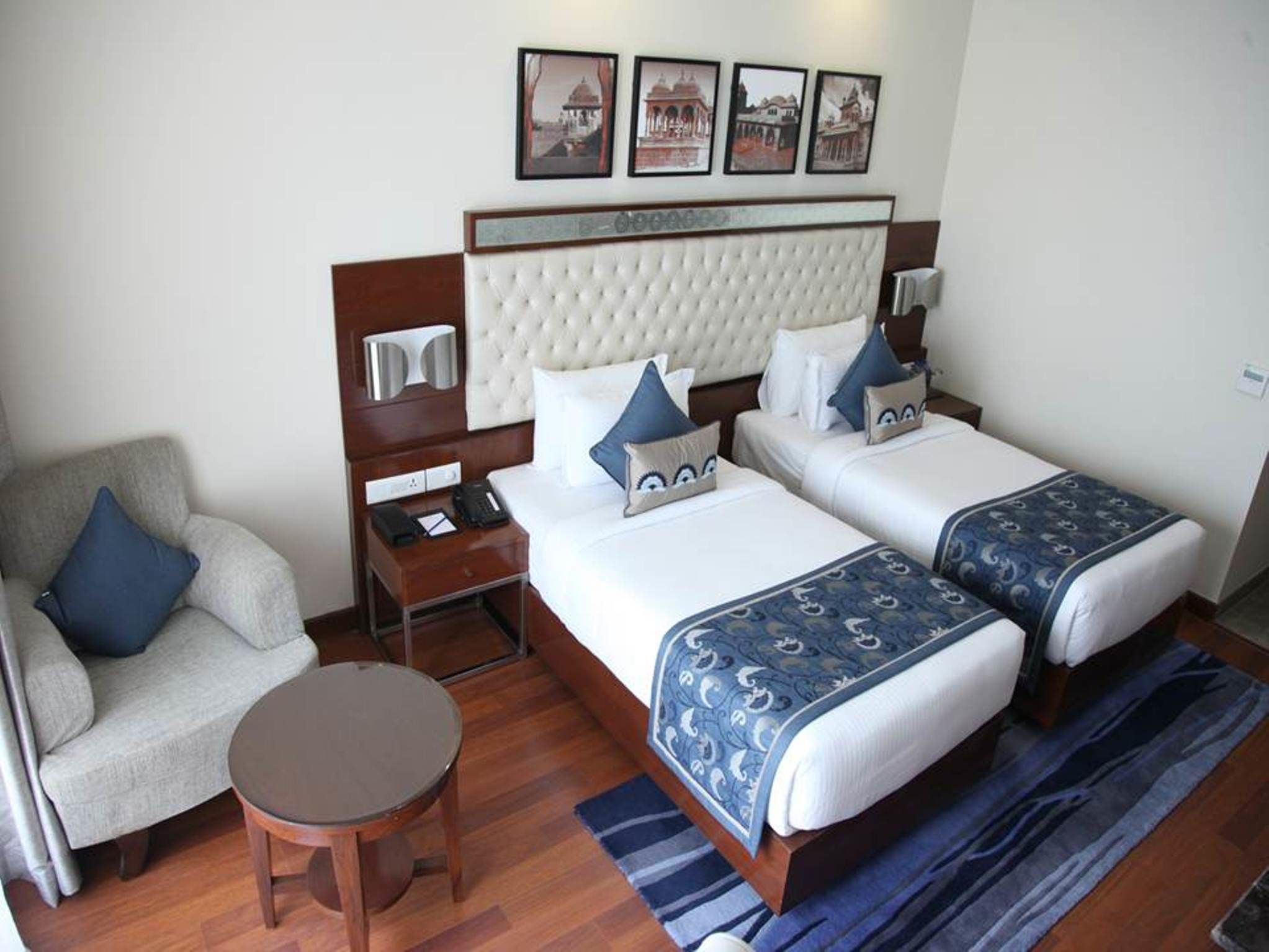 A hotel room with two beds, a sofa, a small table, and a nightstand with a phone and lamp.