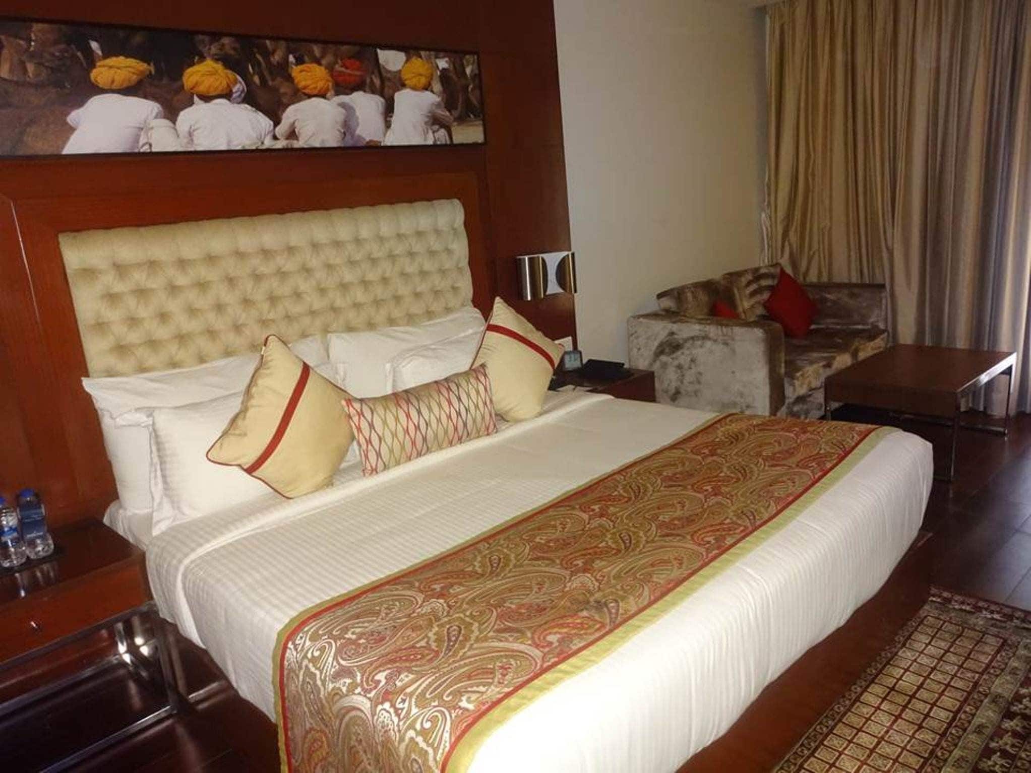 A hotel room with a large bed, a headboard, a nightstand, a sofa, a coffee table, and a painting on the wall.