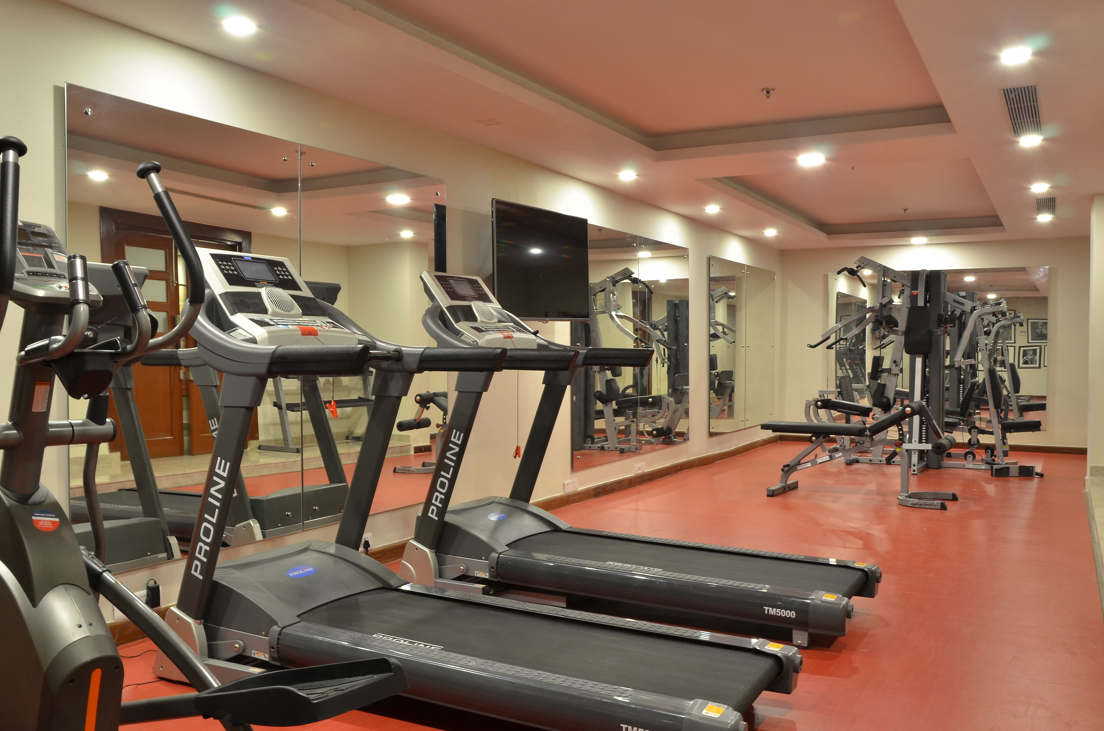 Un gimnasio con cintas de correr, máquinas de pesas y espejos.