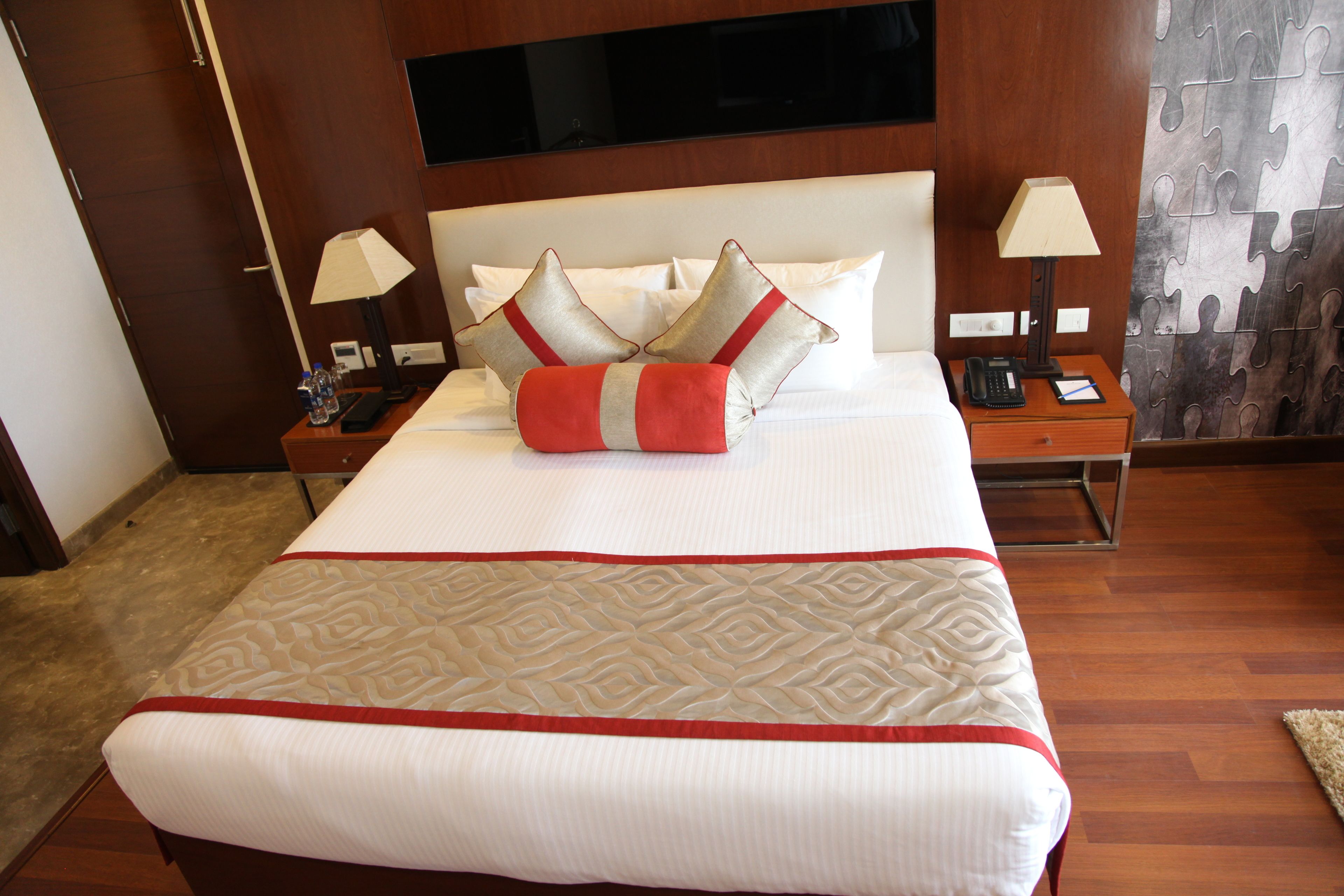 A hotel room with a large bed, two bedside tables, a TV mounted on the wall, and a puzzle-patterned curtain.