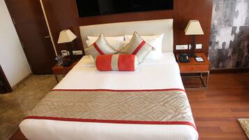 A hotel room with a large bed, two bedside tables, a TV mounted on the wall, and a puzzle-patterned curtain.