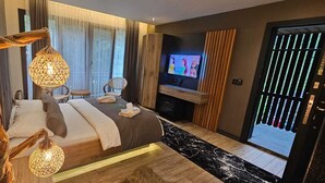 A modern hotel room with a large bed, a television, a small table, and a balcony with a view. - Akyuz Kardesler Hotel & Bungalow (Çaykara)