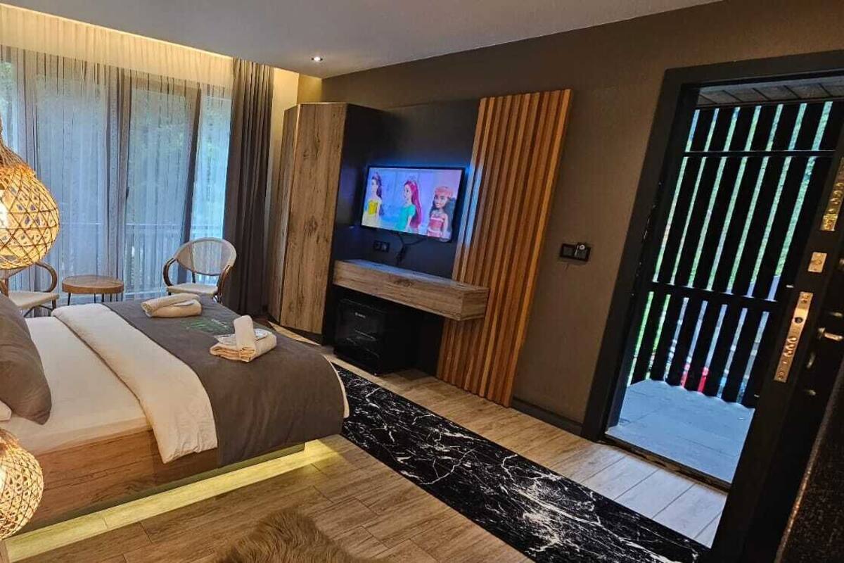 A modern hotel room with a large bed, a television, a small table, and a balcony with a view.