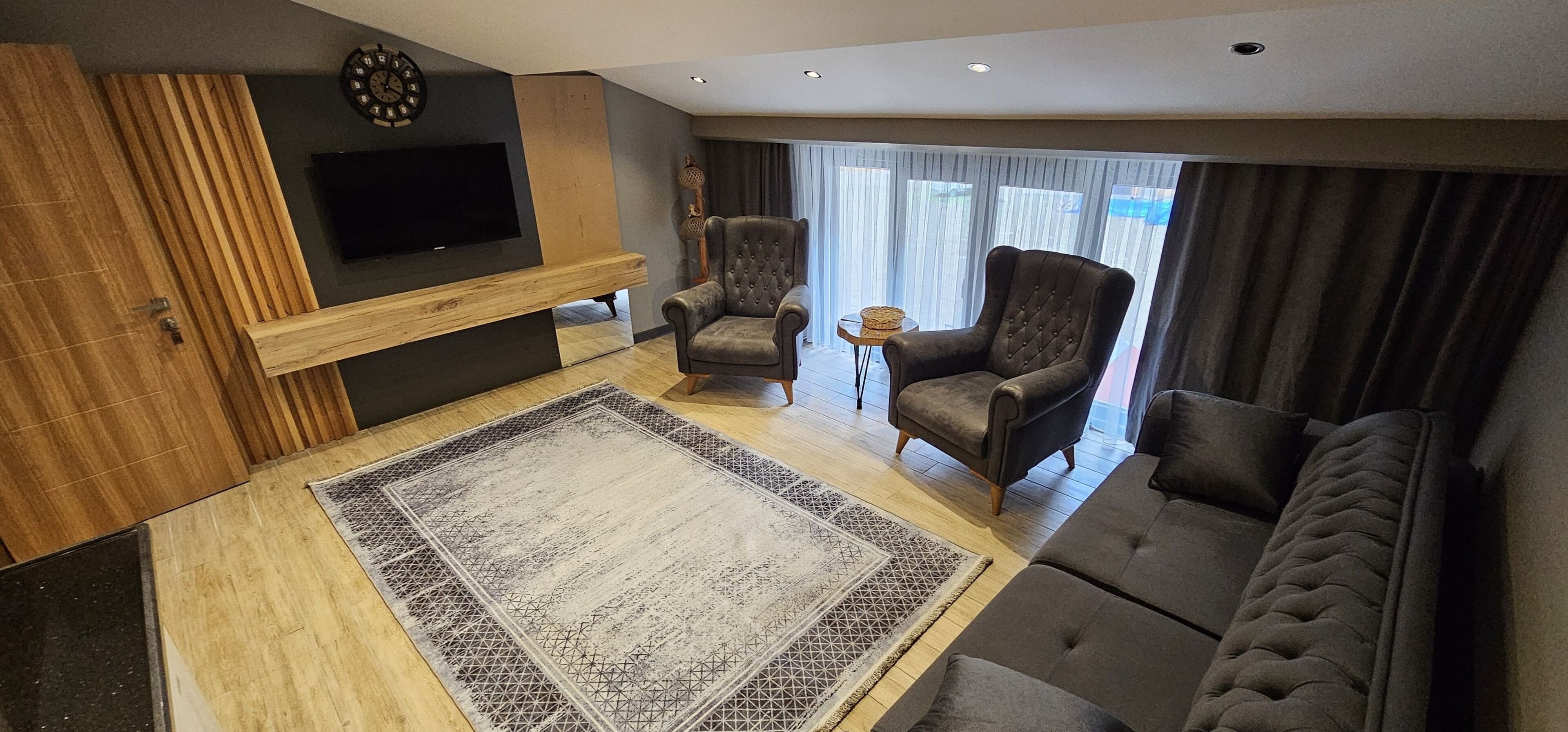 A modern living room with a flat-screen TV, two armchairs, a sofa, and a patterned rug.