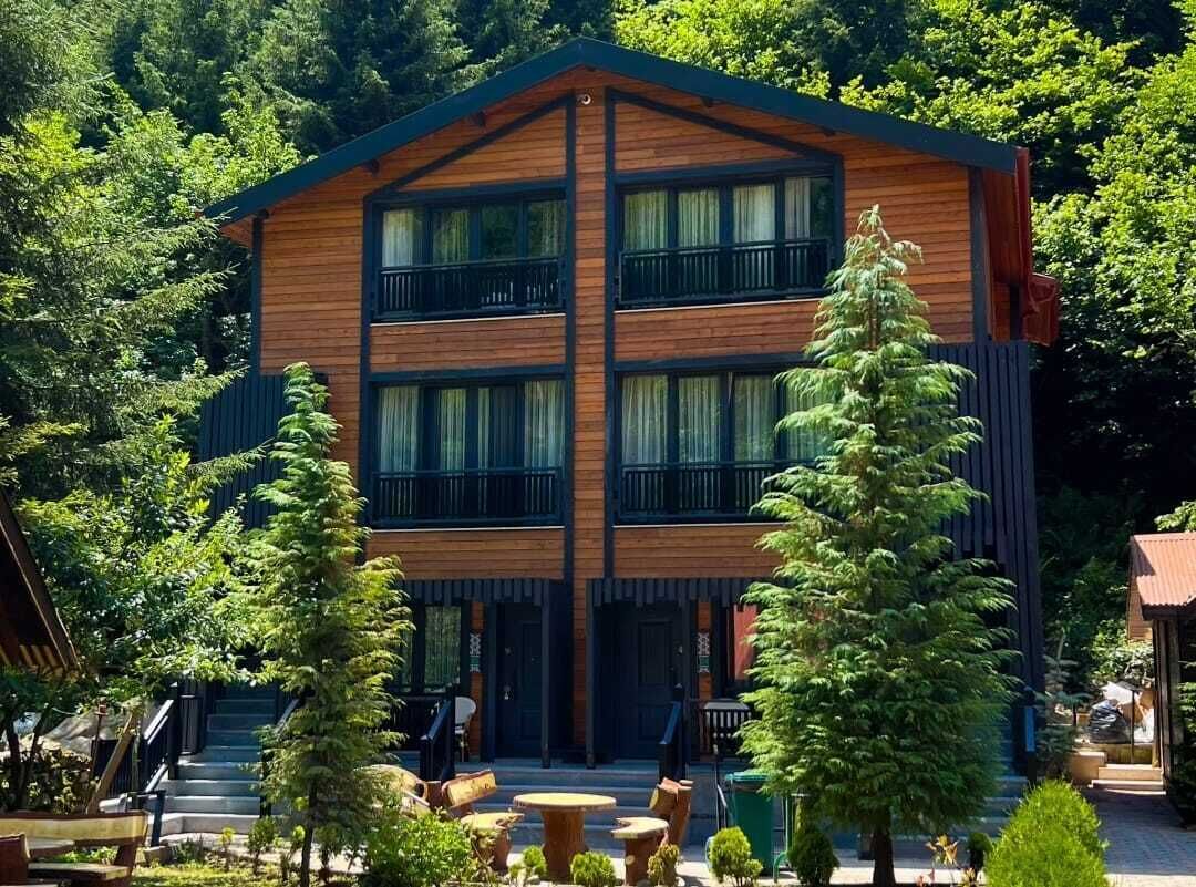 A two-story wooden cabin with balconies, surrounded by trees and outdoor seating.