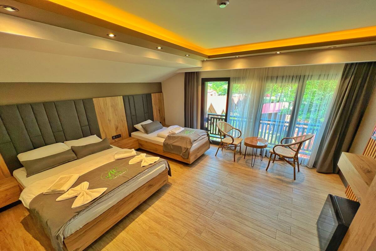 A modern hotel room with a large bed, a smaller bed, a balcony with a table and chairs, and a TV.