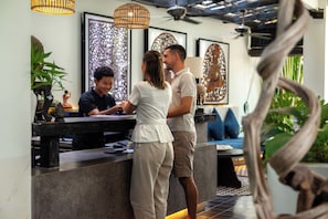 A reception area with a counter, a sofa, and decorative wall art. - Monthara Angkor Residence (Siem Reap)