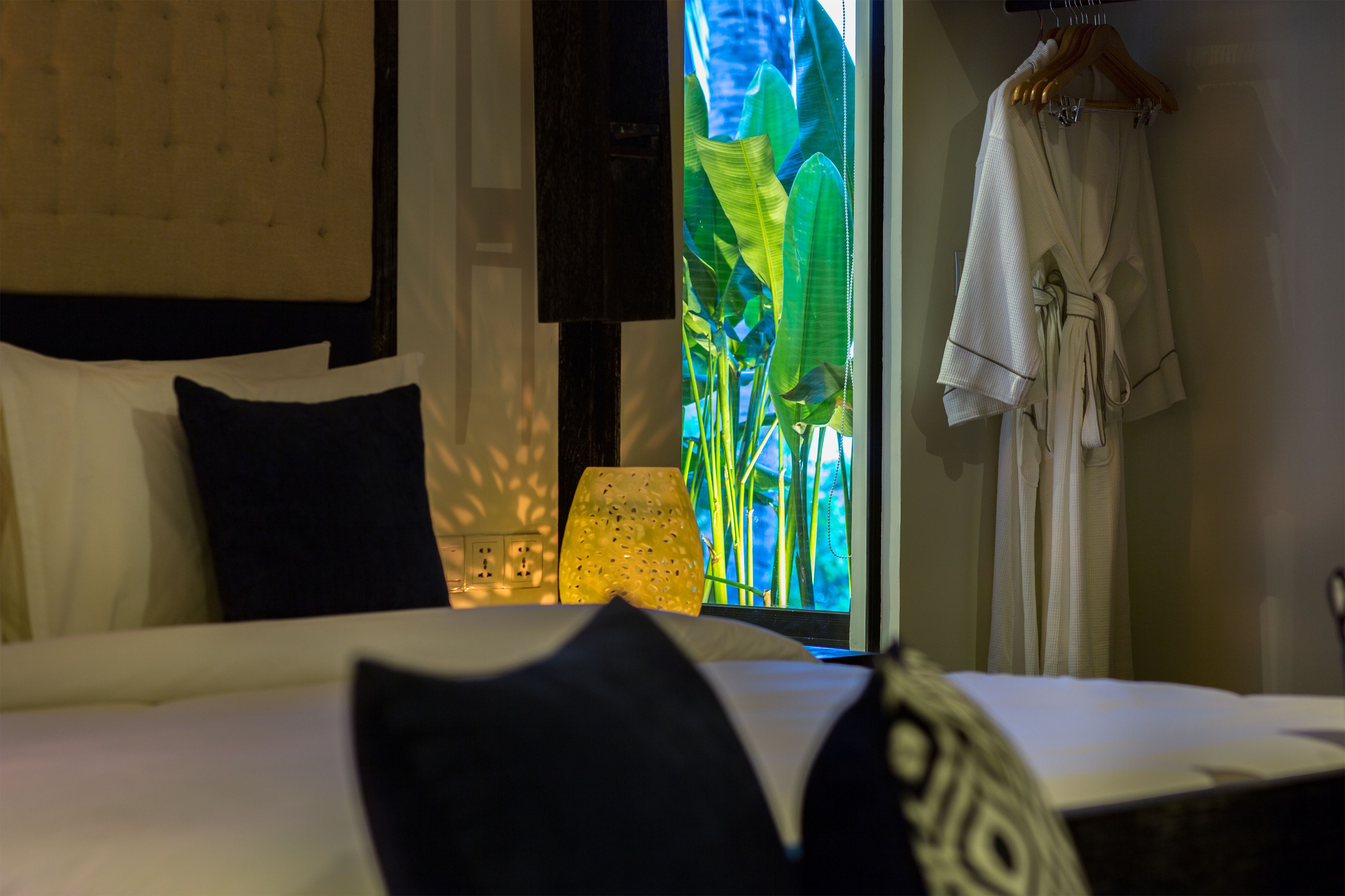 A hotel room with a bed, pillows, a lamp, and a robe hanging on the wall.
