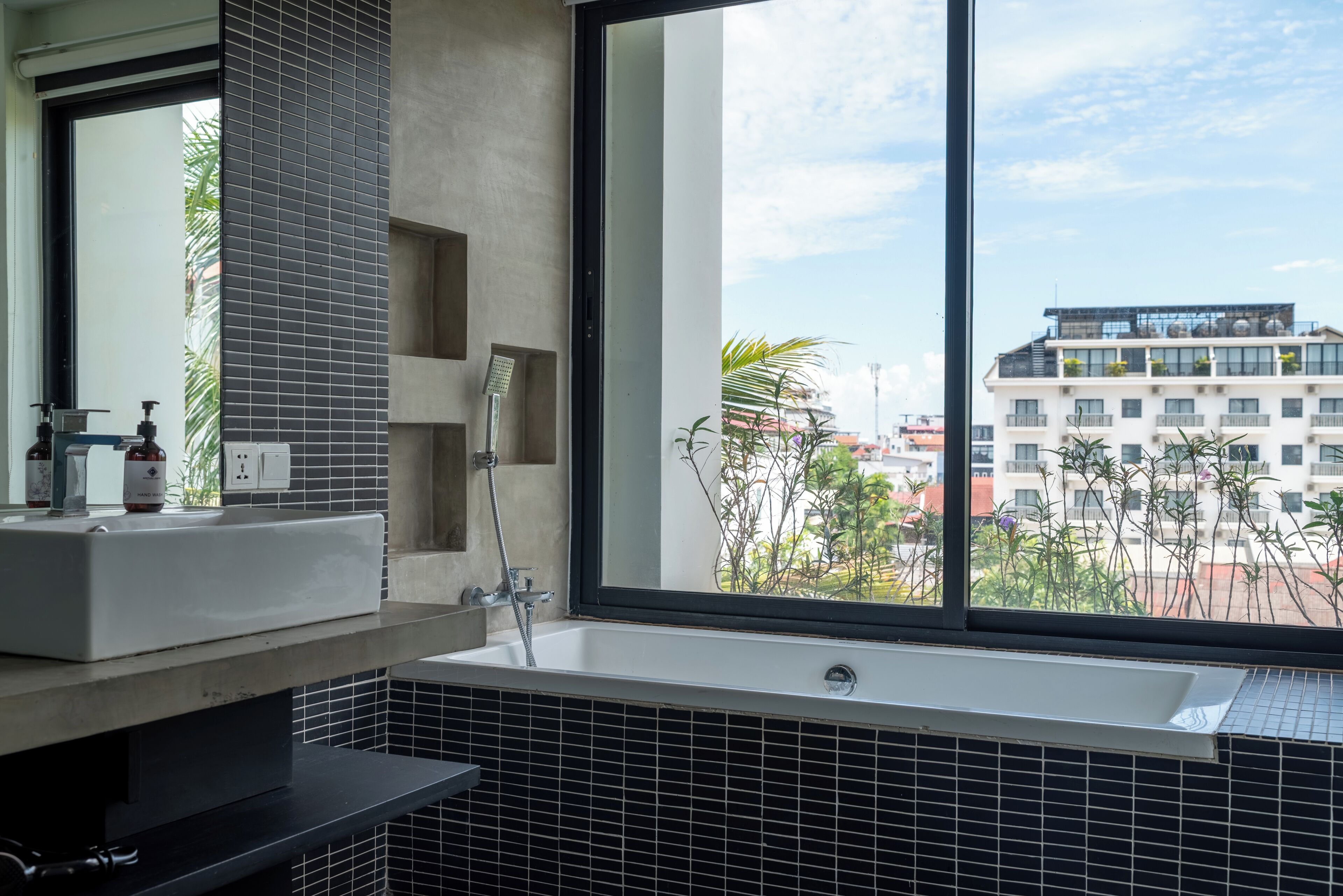 A modern bathroom with a large window, a bathtub, a sink, and a mirror.