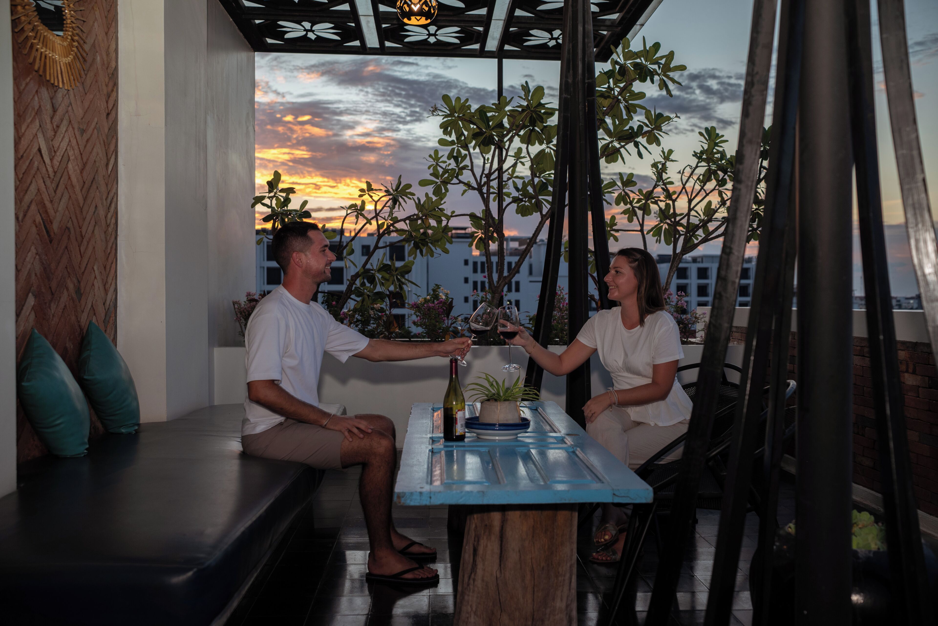 Una pareja sentada a una mesa con vista al atardecer, una botella de vino y una planta en maceta.