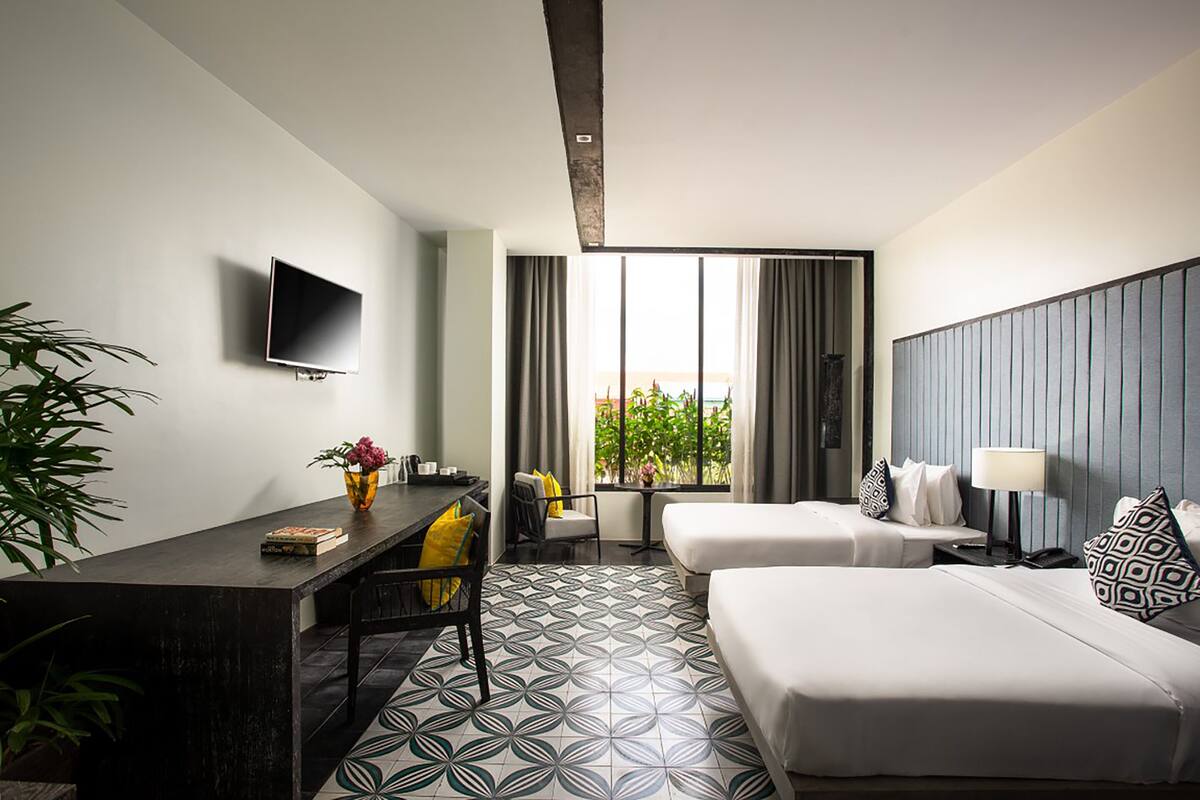 A hotel room with a bed, a desk, a chair, a TV, and a window with curtains.