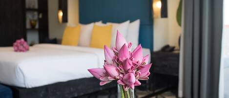 Una cama con ropa de cama blanca, un florero con flores rosas y un suelo estampado.