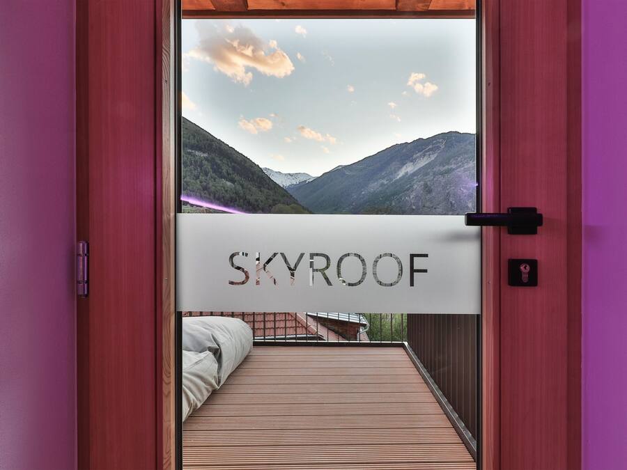 A room with a bed, a window with a view of mountains, and a sign reading "SKYROOF".