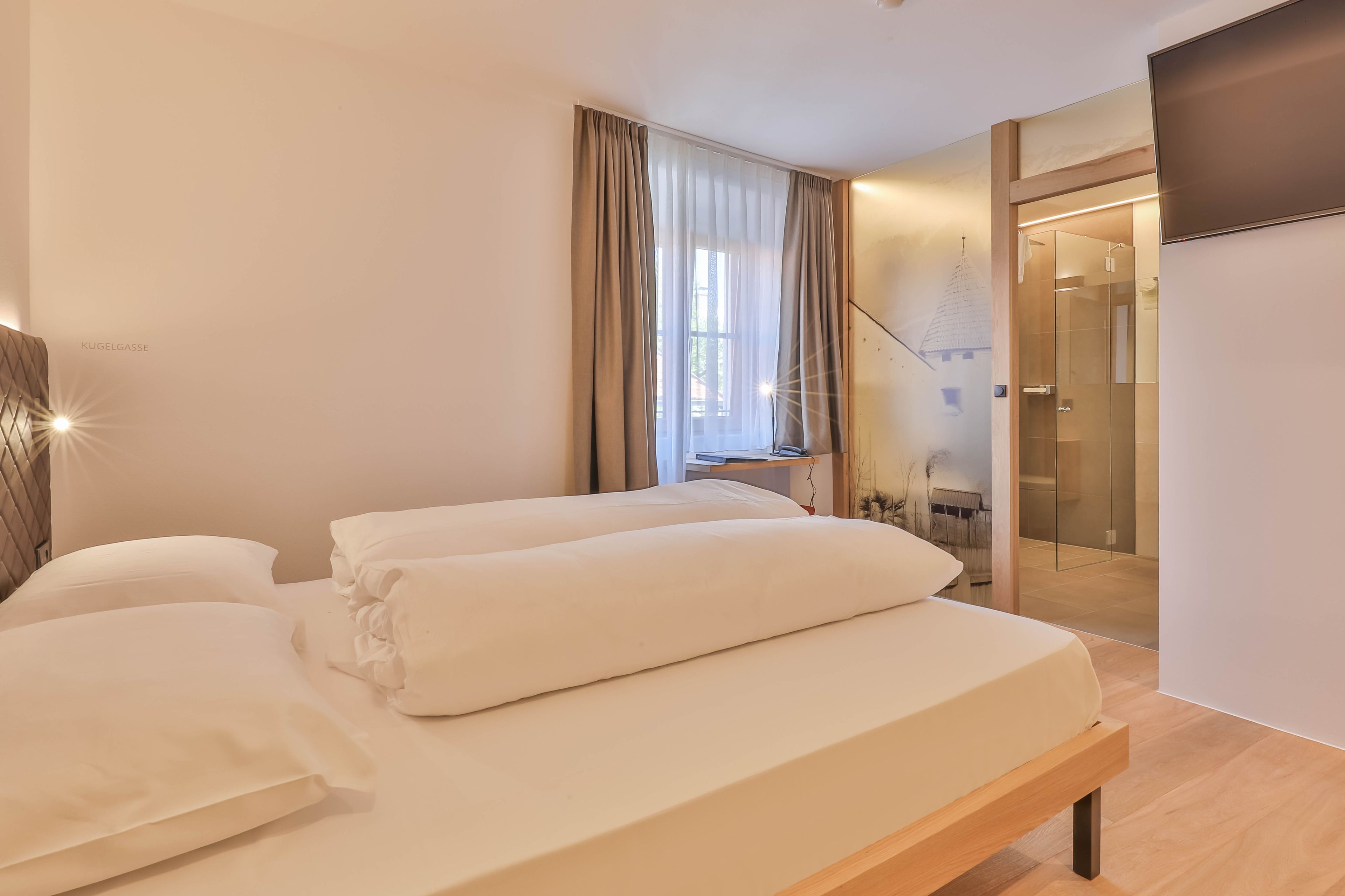 Et moderne hotelværelse med en seng, et skrivebord og en glasdør til et bruseområde.