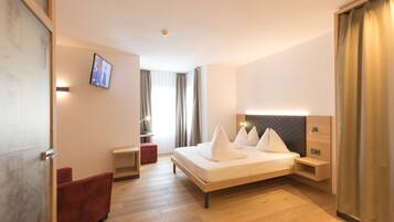 Ein modernes Hotelzimmer mit einem großen Bett, einem Schreibtisch, einem roten Sessel und einem Fernseher an der Wand.