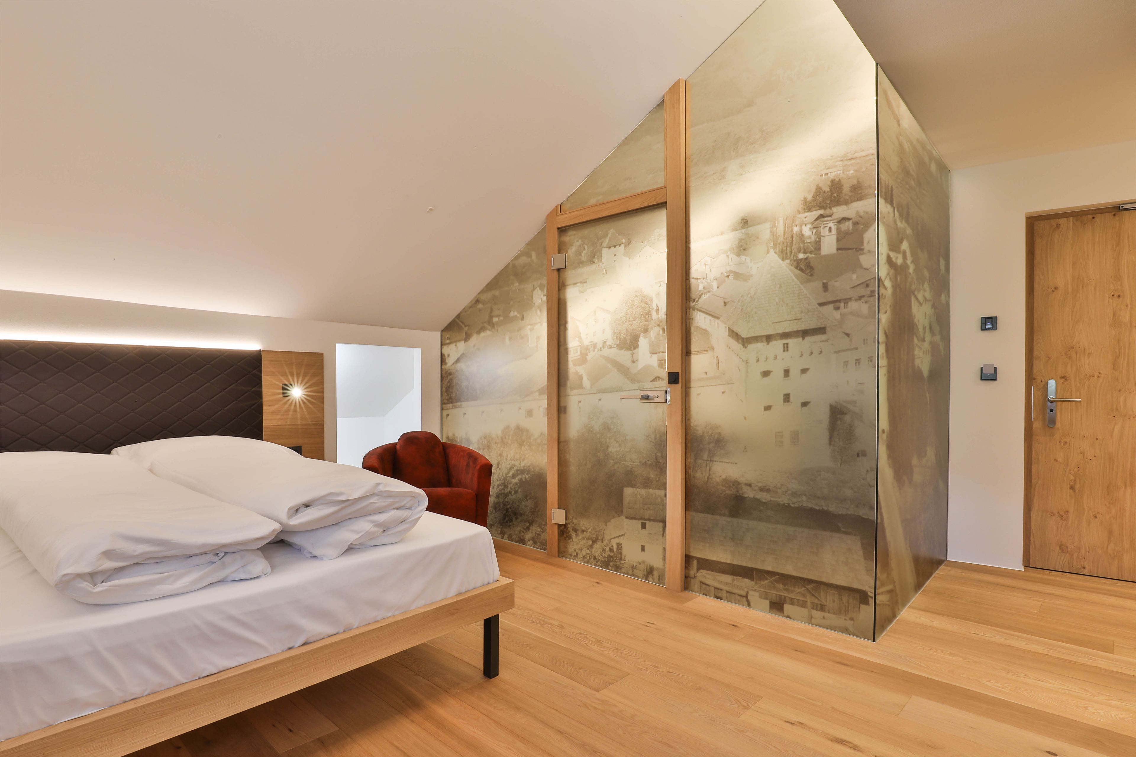 A modern bedroom with a bed, a red chair, and a large glass wall with a cityscape view.