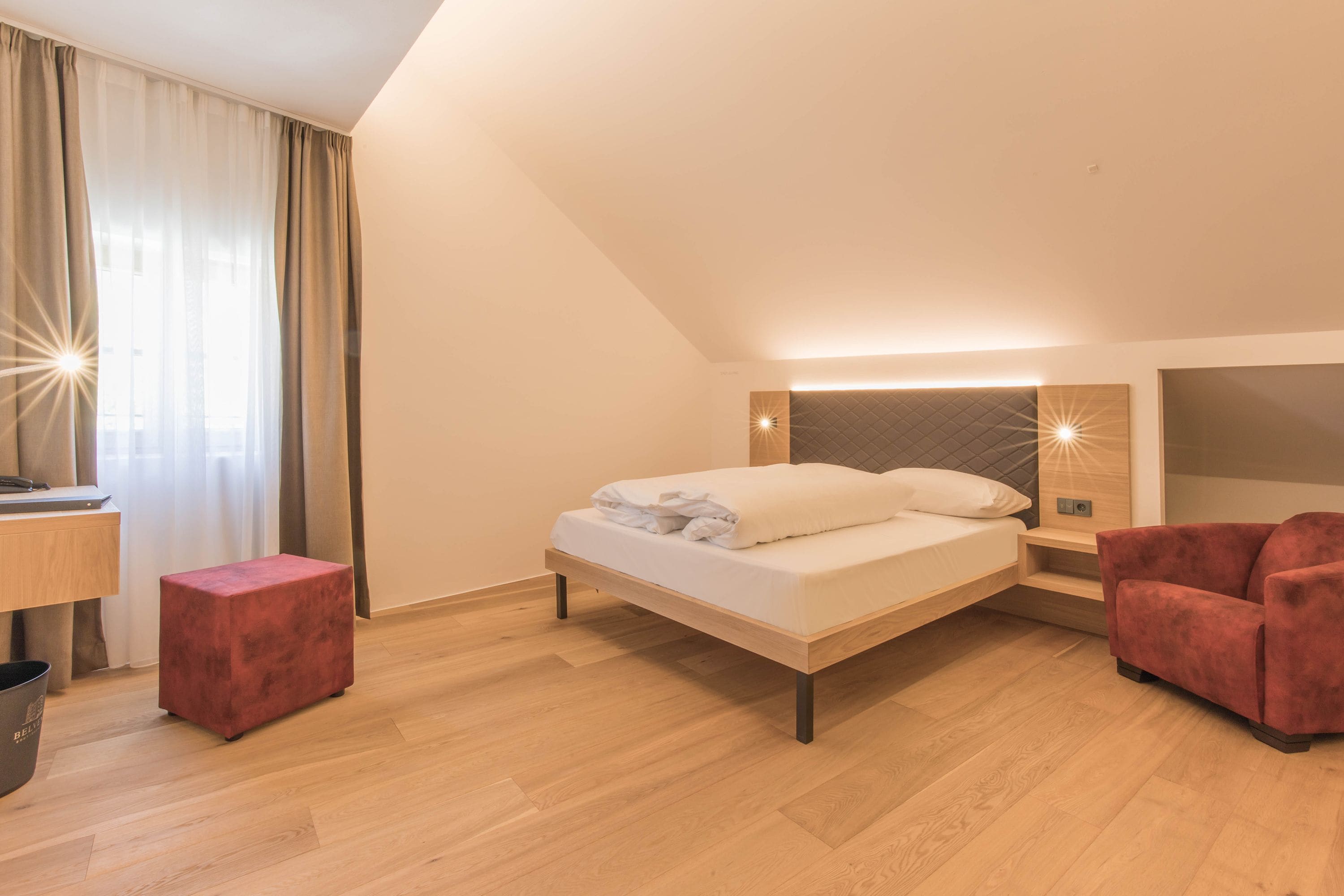 Un dormitorio moderno con cama, un reposapiés rojo, un escritorio y un sillón rojo.