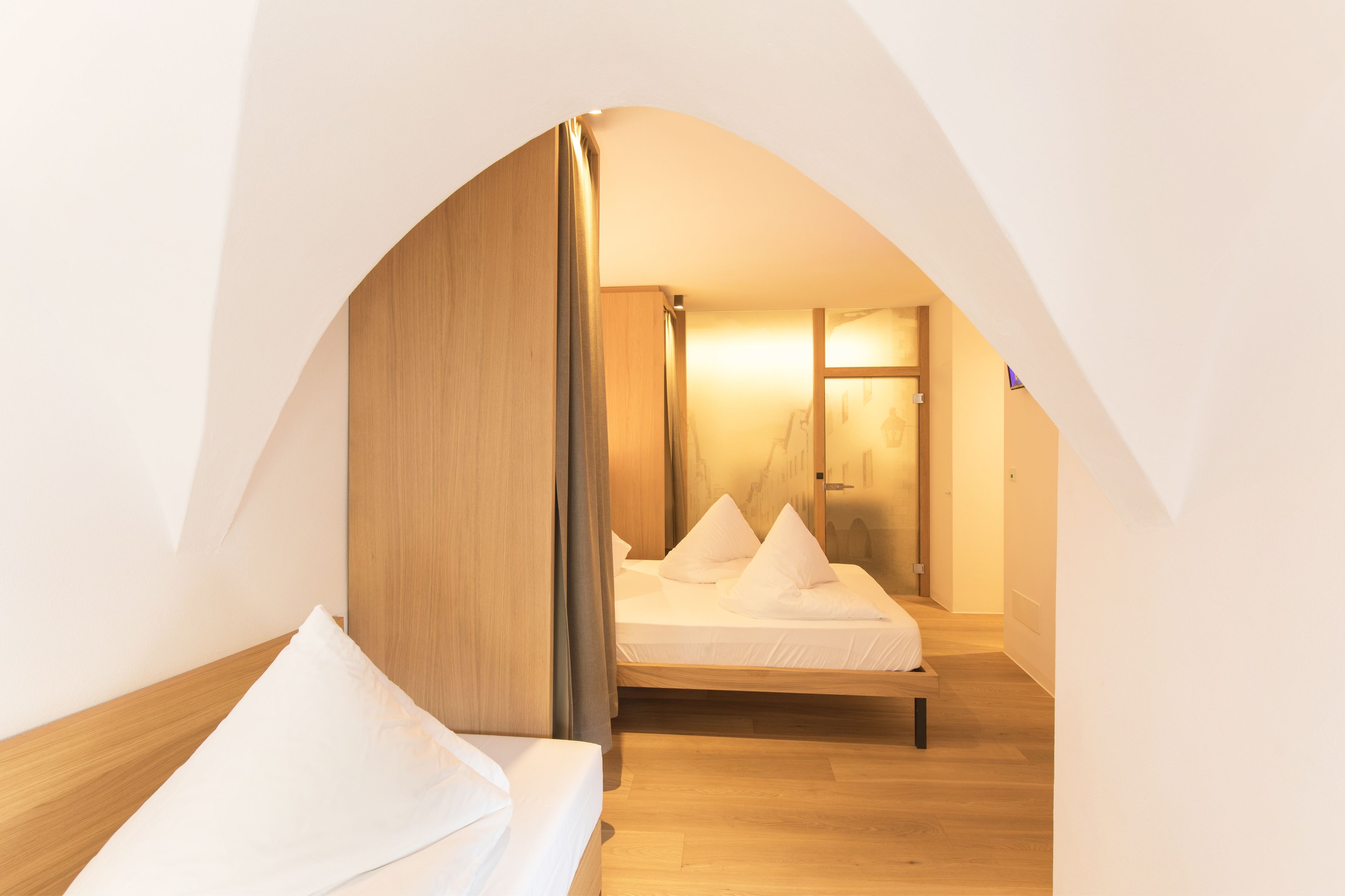 A bedroom with a wooden bed frame, white bedding, and a wooden wardrobe.