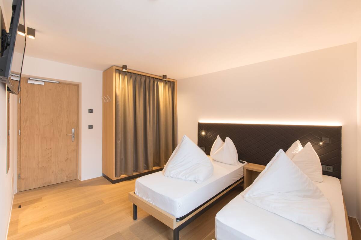 Ein Hotelzimmer mit zwei Betten, einem Holzschrank, einem Vorhang und einem modernen Kopfteil.