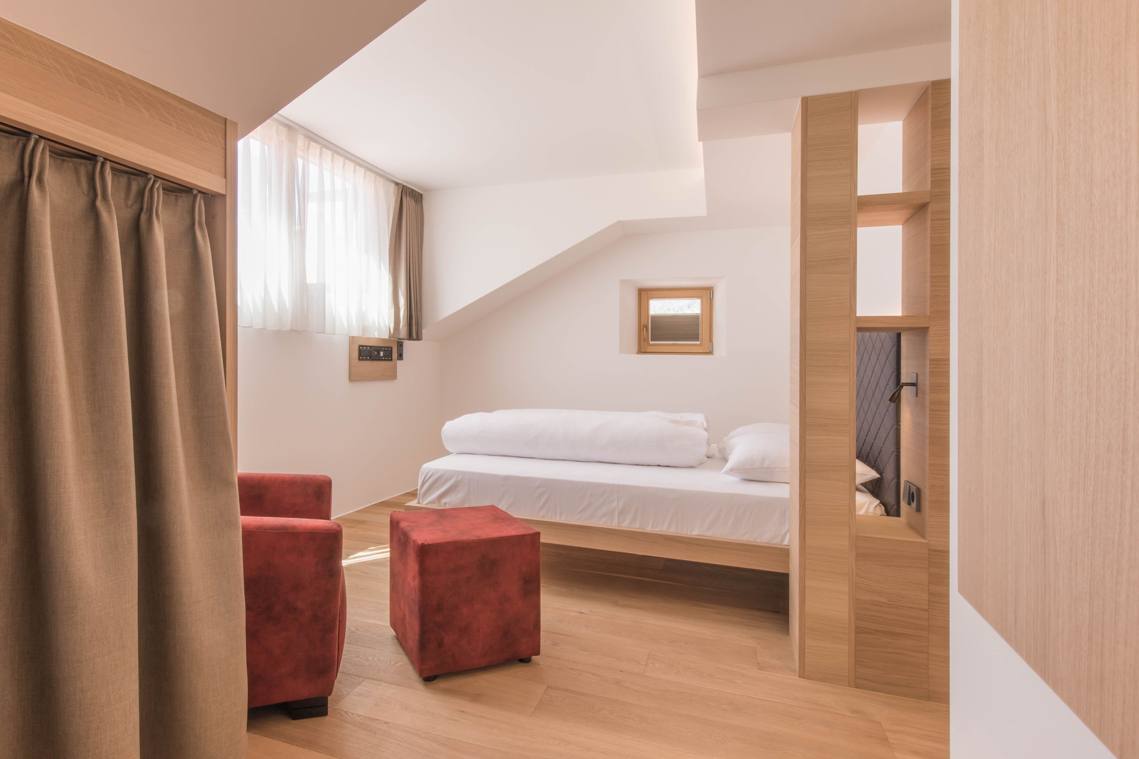 Une chambre moderne avec un lit de style industriel, une petite fenêtre et un pouf rouge.