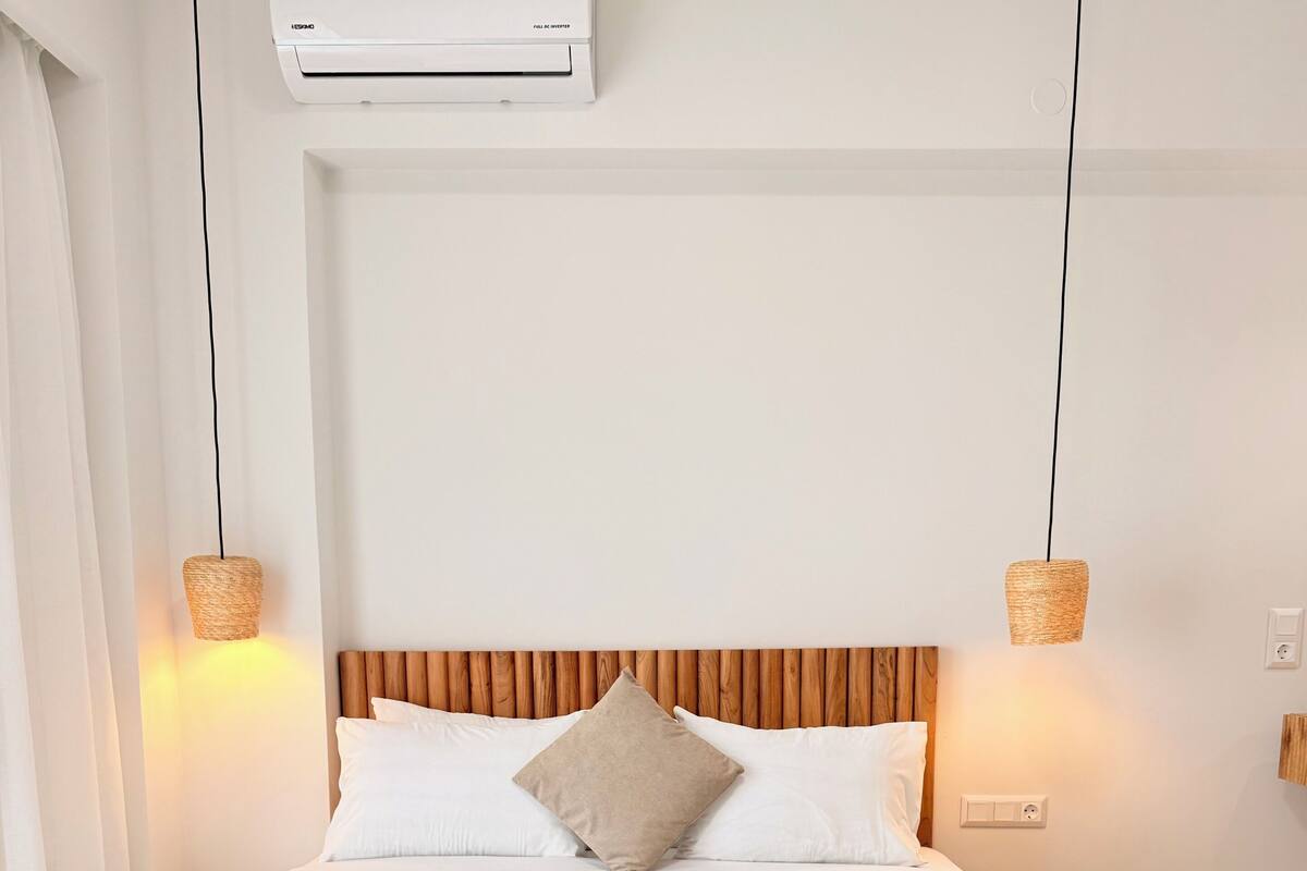 A hotel room with a bed, two bedside lamps, an air conditioner, and a wall socket.
