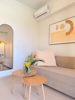 Una sala de estar moderna con un sofá, una mesa redonda de madera, un espejo y una obra de arte enmarcada en la pared.