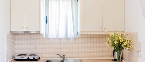 A compact kitchen with white cabinets, a stainless steel refrigerator, a sink, and two stools.