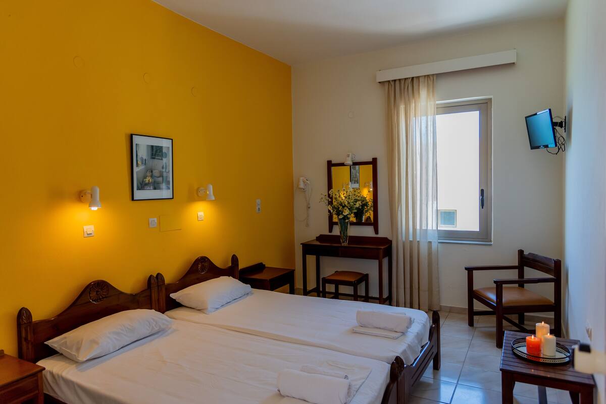 A hotel room with two beds, a desk, a chair, a TV, and a window with curtains.