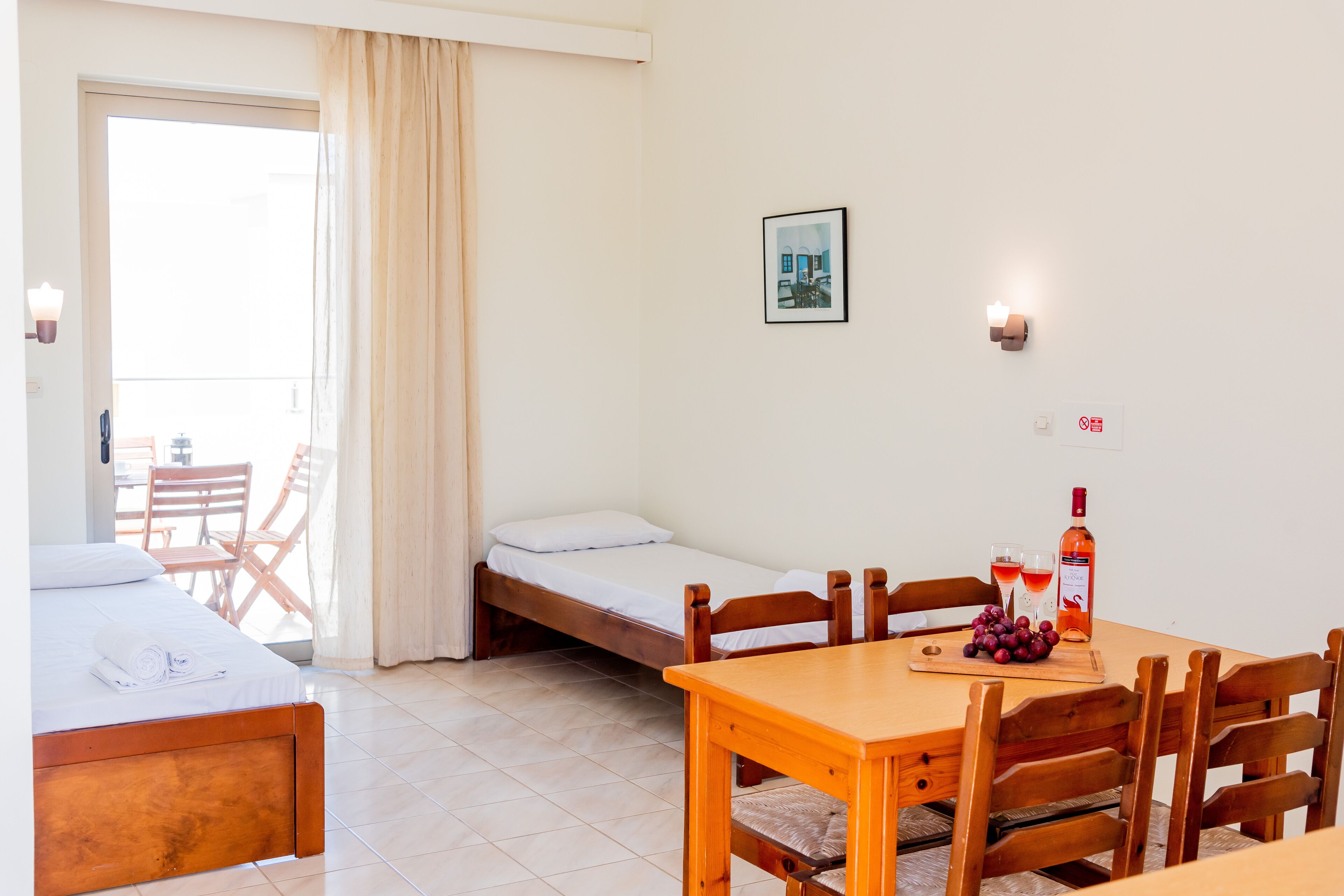 A room with a bed, a small table with a bottle and glasses, and a chair.