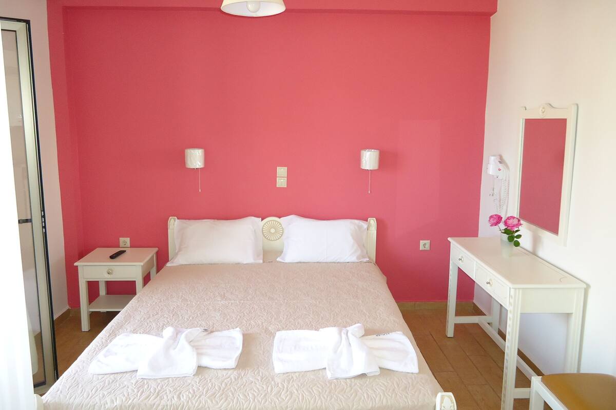 A bedroom with a large bed, a bedside table, a desk, and a mirror.