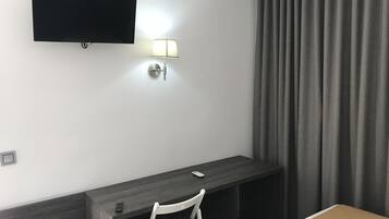 A hotel room with a flat-screen TV mounted on the wall, a desk with a chair, a lamp, and a bed.