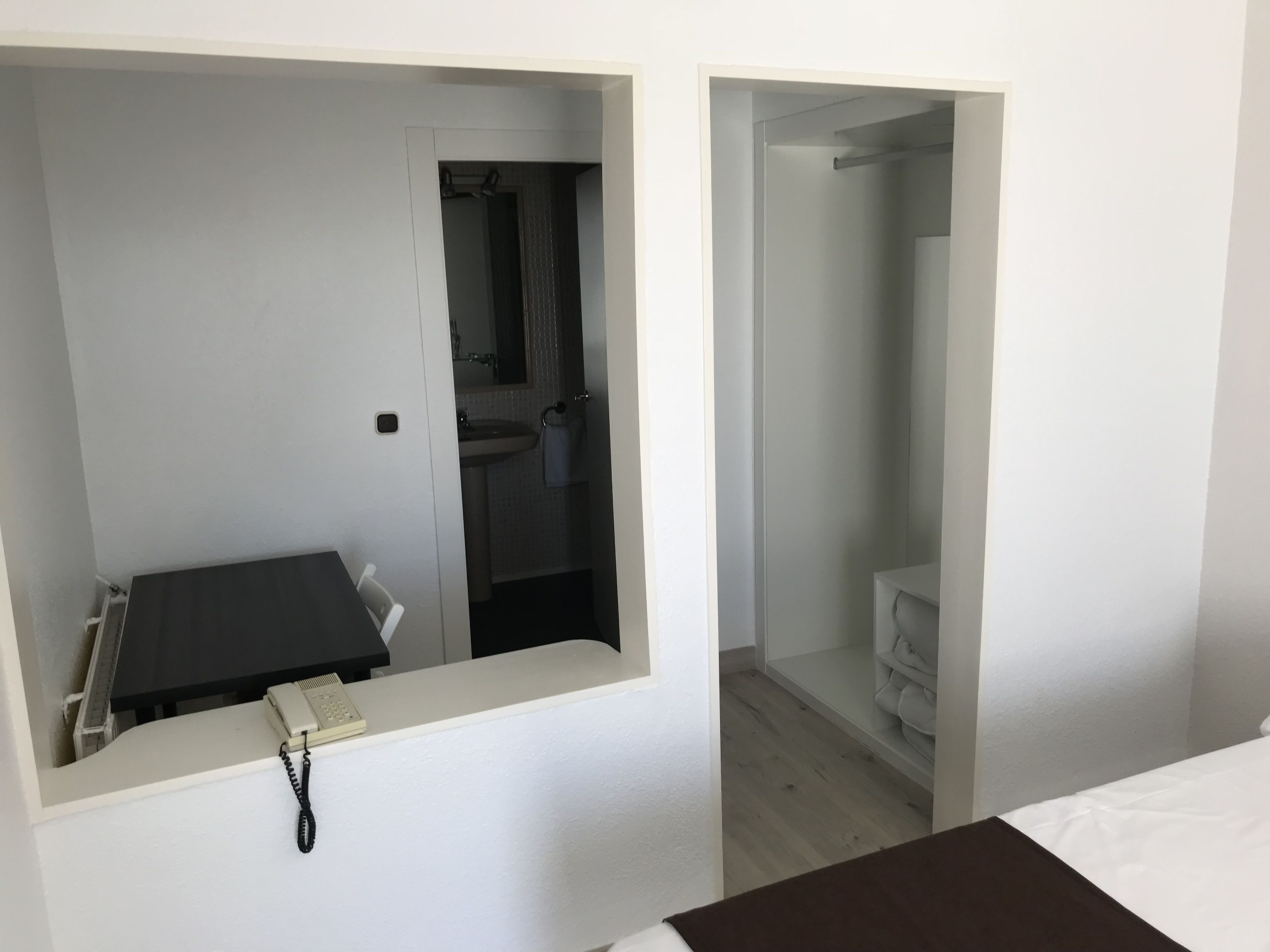 Une chambre d’hôtel comprenant un lit, un bureau avec un téléphone et une salle de bain avec un lavabo et un miroir.