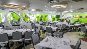 Un restaurante con varias mesas y sillas, paredes verdes y luces en el techo.