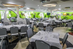 Un restaurante con varias mesas y sillas, paredes verdes y luces en el techo.
