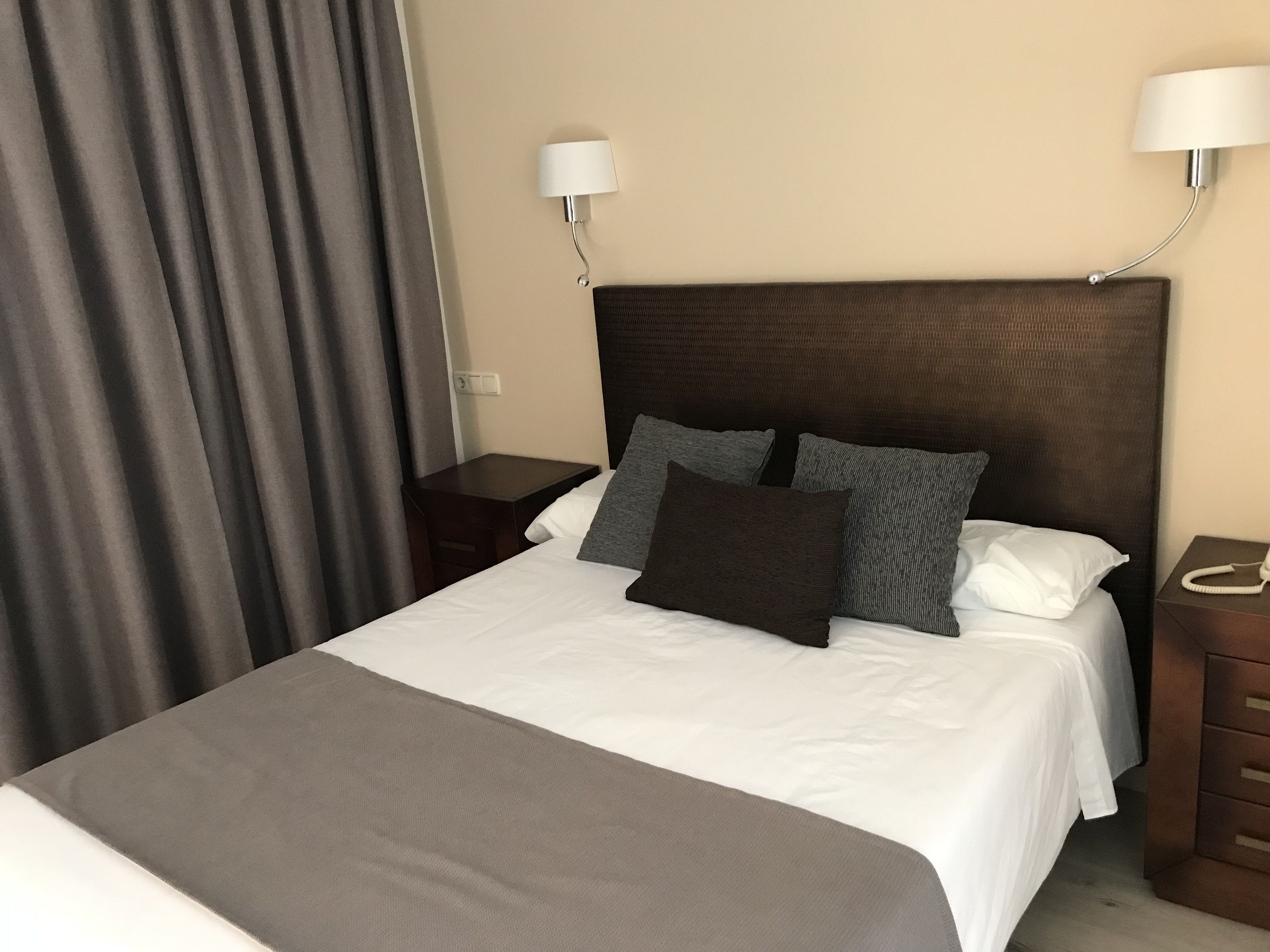 Una cama bien hecha con un cabecero marrón, dos mesitas de noche y una lámpara a cada lado.