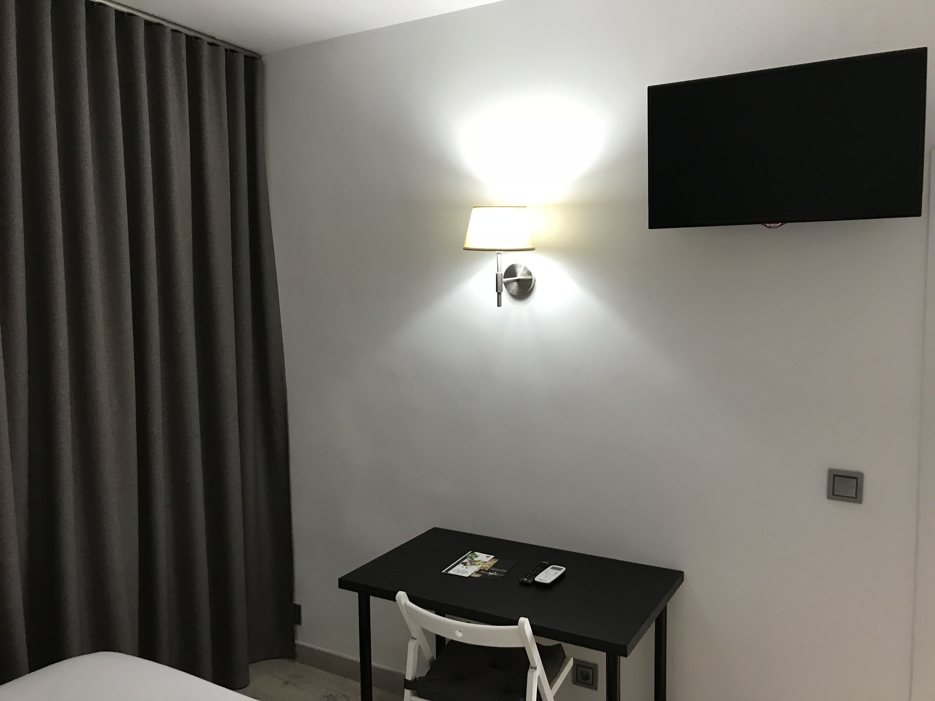 A hotel room with a bed, a desk, a lamp, a TV, and a window with curtains.