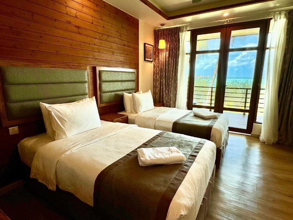 A hotel room with two beds, wooden walls, a large window with a view, and a nightstand with a lamp.