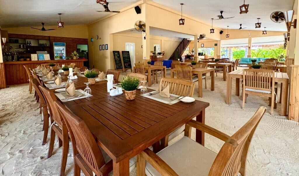 Een restaurant aan het strand met houten tafels en stoelen, een bar en uitzicht op het strand.
