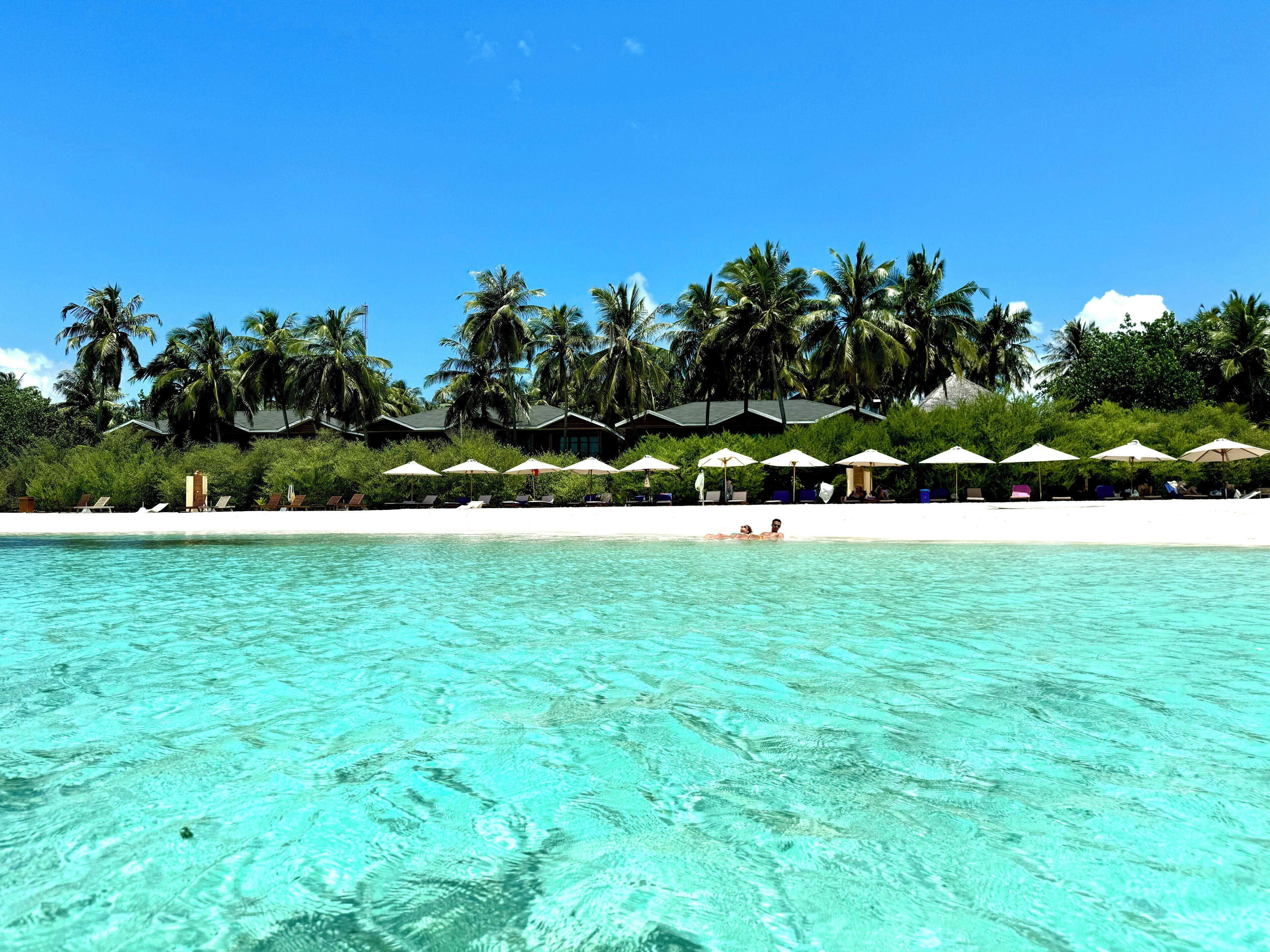 Un resort en la playa con aguas turquesas cristalinas, palmeras y sombrillas.