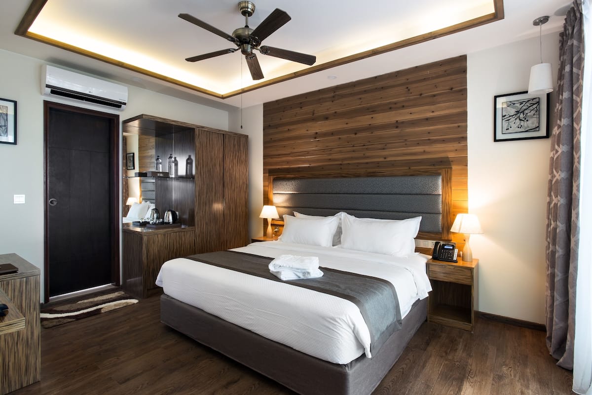 Une chambre d’hôtel avec un grand lit, une tête de lit en bois, des lampes de chevet, un ventilateur de plafond et une armoire.