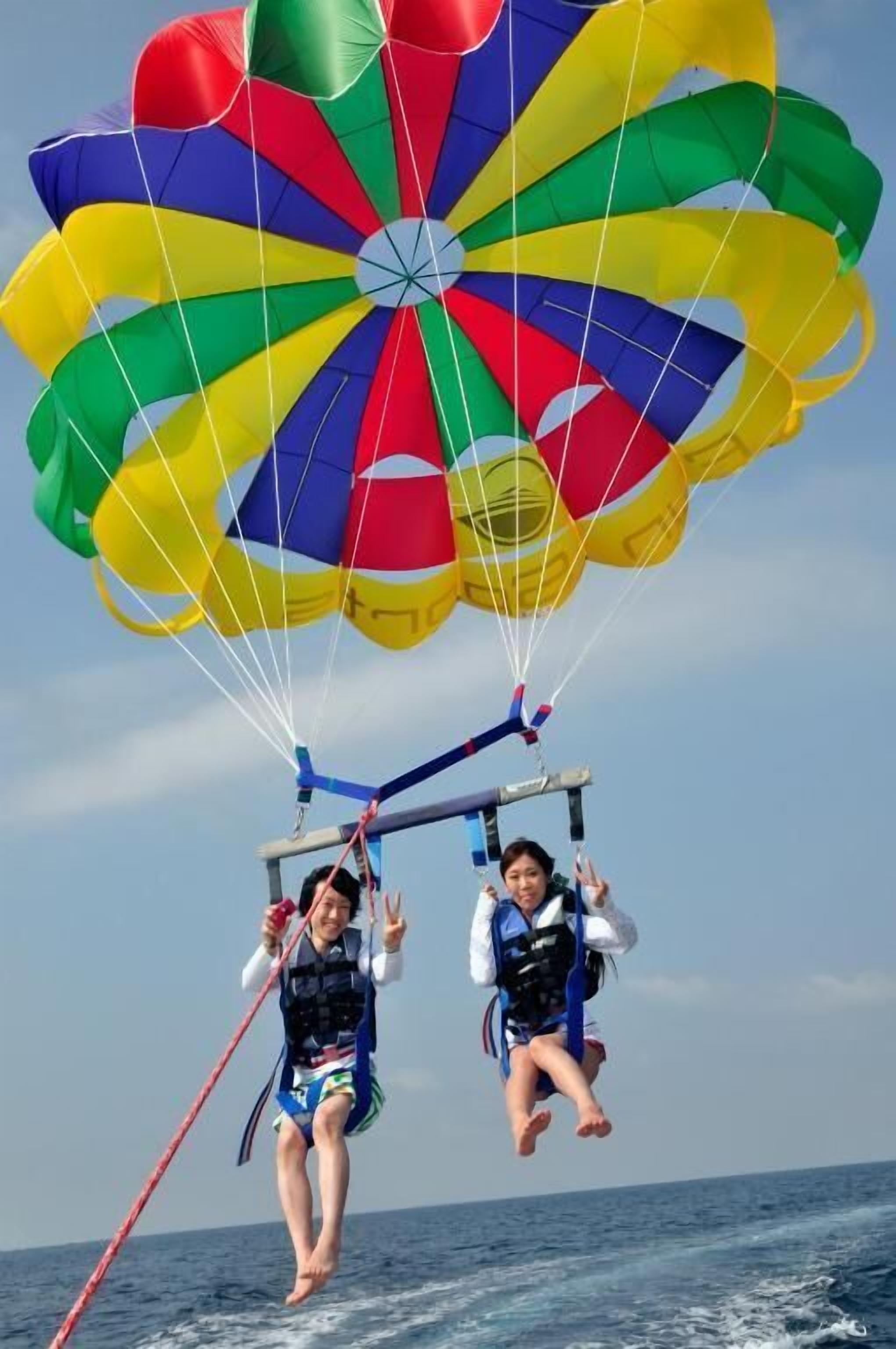 Dos personas parapenteando sobre el agua con un paracaídas colorido.