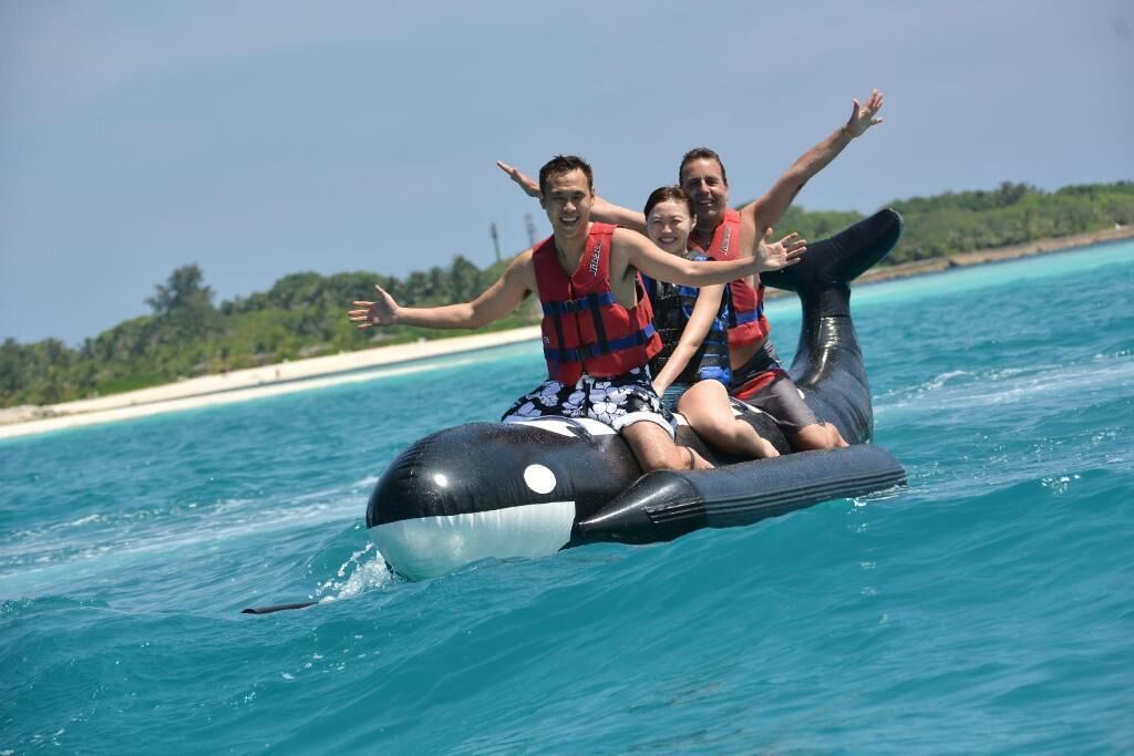 Three people on a black and white inflatable orca-shaped watercraft.