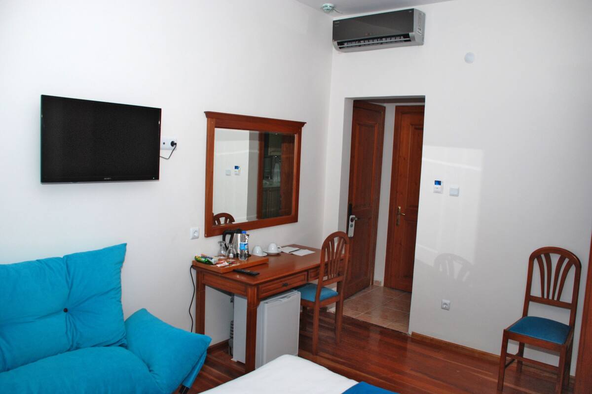 A hotel room with a bed, a desk, a chair, a TV mounted on the wall, and a door leading to another room.