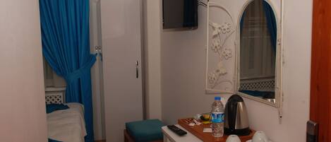 A hotel room with a bed, a small table with a remote control, a water bottle, and a mirror with a floral design.